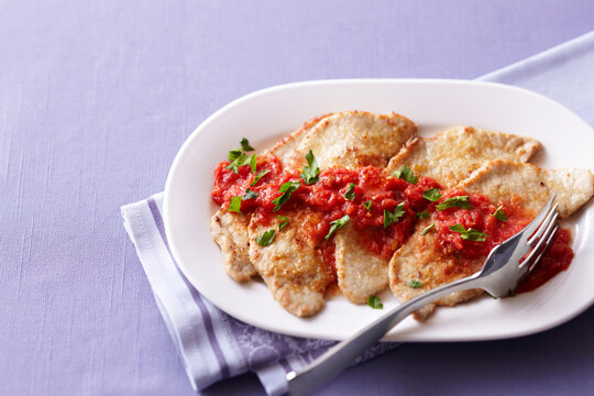 Veal with tomato sauce on a white platter on a purple background