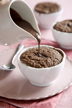Individual chocolate souffle with chocolate sauce poured on top on a pink background