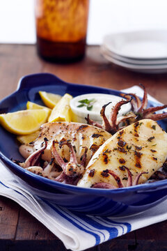 Grilled calamari with lemon wedges in a blue bowl