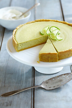 Avocado Cheesecake Topped With Limes On A Cake Stand With A Slice Cut Out