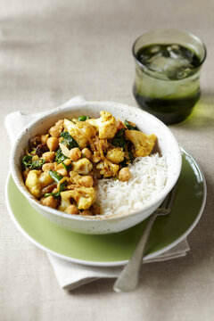 Bowl of cauliflower, chickpea and spinach curry with white rice and a glass of water