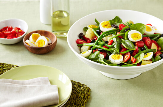 Nicoise Salad with eggs, green beans, tomatoes and olives on a green linen tablecloth