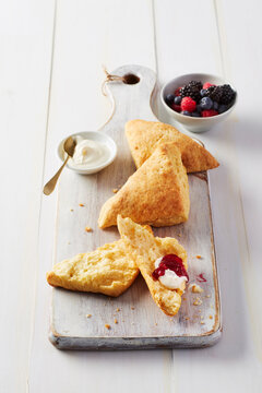 Fresh scones on a cutting board with clooted cream and side dish of berry