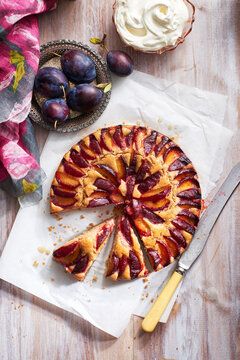 Plum cake with fresh plums and whipped cream with piece taken out and serving knife