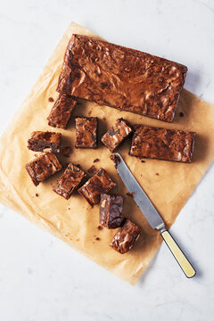 Brownies with toffee chunks cut into pieces on parchment paper with a knife