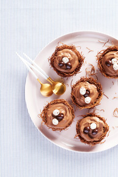 Plate of chocolate mousse nest cups with chocolate egg garnish and gold colored spoons