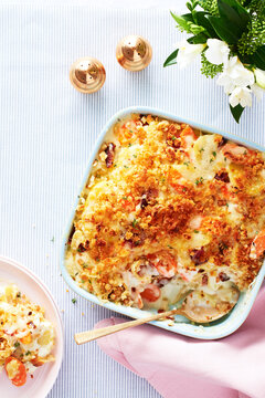 Root vegetable gratin in a square dish and serving spoon with pink napkin and blue striped background