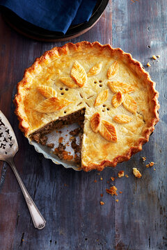 Tourtiere with a decorated crust and one piece taken out on a blue wooden background