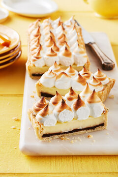 Lemon meringue tart with chocolate fudge layer cut into pieces on cutting board