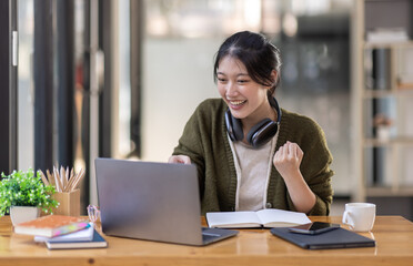 Fototapeta na wymiar Young adult happy smiling Hispanic Asian girl student wearing headphones talking on online chat meeting using laptop in university campus or at virtual office. College female student learning remotely