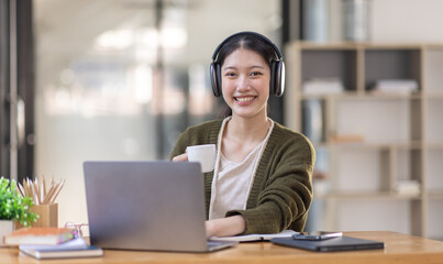 Young adult happy smiling Hispanic Asian girl student wearing headphones talking on online chat meeting using laptop in university campus or at virtual office. College female student learning remotely