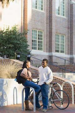 Young man and young woman outdoors on college campus, talking next to bike rack, Florida, USA
