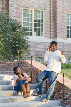 Young man and young woman outdoors on college campus steps, young man using smartphone, Florida, USA