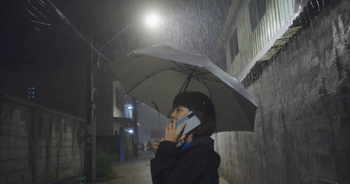 On a rainy day, an Asian woman stands alone in an alley. she using a mobile phone