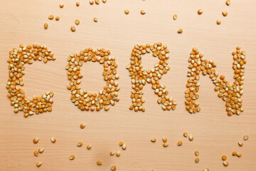 Pile of yellow corn seeds form the word 'CORN' on a brown wooden background, for popcorn.