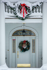 Gold and white front door decorated with Christmas decorations and snow