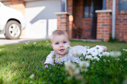 Happy baby from young Caucasian family on front yard grass outside of home