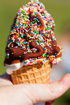 sunlit hand holding waffle cone with soft serve ice cream dessert