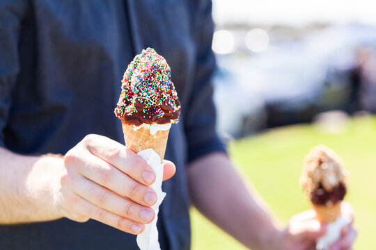 Person holding out soft serve ice cream with chocolate topping and sprinkles on summers day