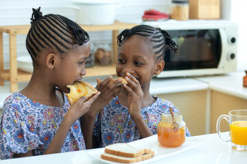 Twin African girls enjoying toast with marmalade in modern kitchen, delicious together
