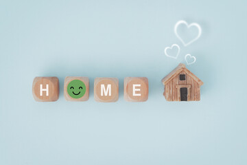 HOME text with smiling face instead of O on wooden cube block and miniature wood house with blurred white heart above , for warm family, nursery home care, foster house concept