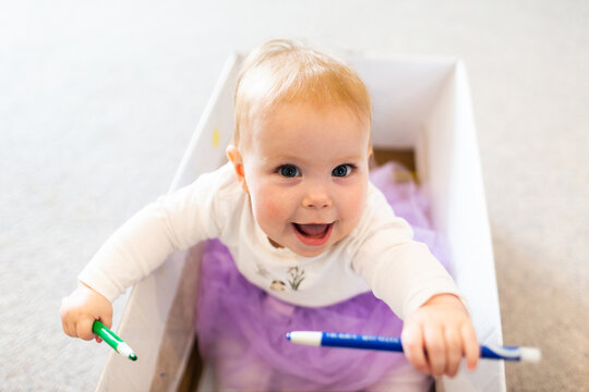 Baby girl sitting in box drawing with crayon textas at home