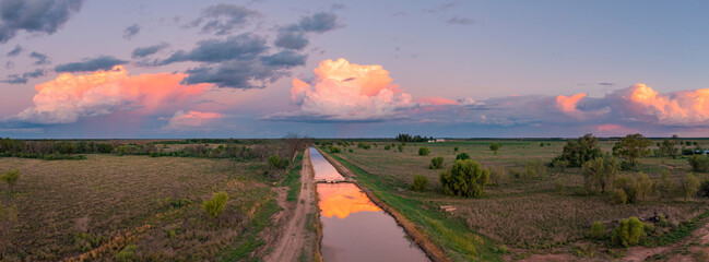 Aerial view of colourful storm clouds at twilight reflected in the water of an irrigation channel