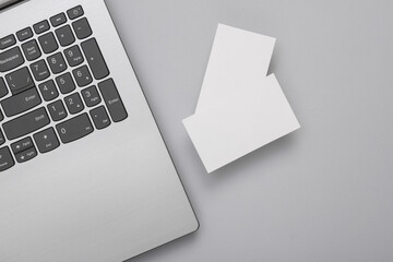 Two white Blank business cards for branding and laptop on gray background. Top view. Business concept
