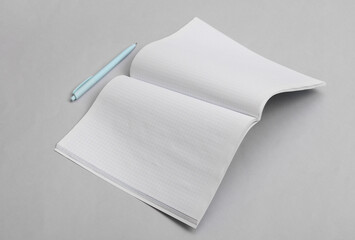 Open Notebook (exercise book) or journal (magazine) with white papers and pen on gray background....