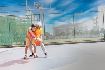 Grandfather and his grandson enjoying and playing together on basketball court.