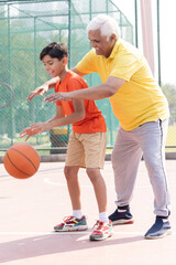 Grandfather and his grandson enjoying and playing together on basketball court.