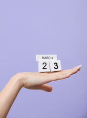 Block calendar with date march 23 on female palm, pastel color lavender background