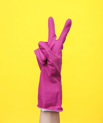 Hand in purple rubber cleaning glove shows v symbol on a yellow background. House cleaning and...