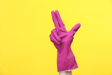 Hand in purple rubber cleaning glove on a yellow background. House cleaning and housekeeping concept