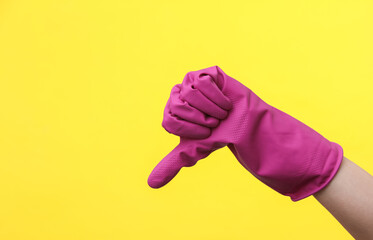 Hand in purple rubber cleaning glove shows thumbs down on a yellow background. House cleaning and...