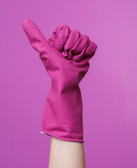 Hand in purple rubber cleaning glove shows thumbs up on purple background. House cleaning and housekeeping concept