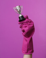 Hand in purple rubber cleaning glove holding cup trophy on purple background. House cleaning and housekeeping concept
