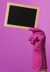 Hand in purple rubber cleaning glove holding empty chalk board on purple background. House cleaning and housekeeping concept