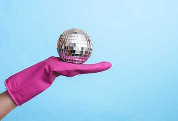 Hand in purple rubber cleaning glove holding disco ball on blue background. House cleaning and...