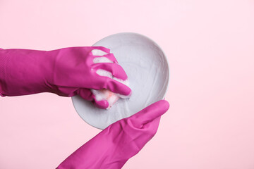 Hands in rubber gloves wash plate on pink background