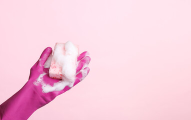 Woman's hand in glove holds sponge in foam on a pink background. Cleaning concept