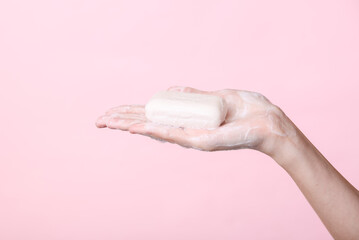 Woman's hand holds foaming soap on pink background. Hygiene, clean hands