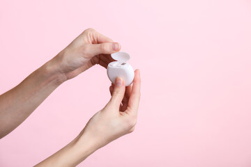 Female hands holding a box of dental floss on a pink background. Dental care