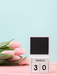 Block wooden calendar with the date March 30 and tulips on a pastel background. Spring composition