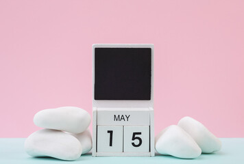 Block wooden calendar with the date may 15 and white pebbles on pastel background.