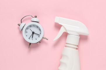 Detergent spray bottle with alarm clock on pink background. Creative layout. Cleaning concept