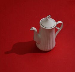 Ceramic teapot on a red background with a shadow. Minimalism style.