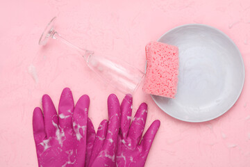 Sponge, plate and glass, rubber gloves with foam on a pink background. Washing dishes concept. Top view