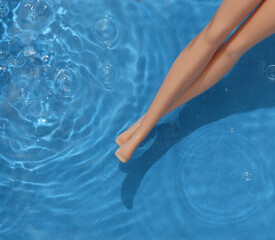 Fototapeta na wymiar Doll legs in blue water with shadows. Beach rest. Top view