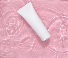 Obraz na płótnie Canvas White cream tube in pink water with shadows. Beauty concept. Top view